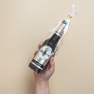 Eine Flasche Schokoladenbier in Geschenkfolie verpackt in einer Hand pr&auml;sentiert