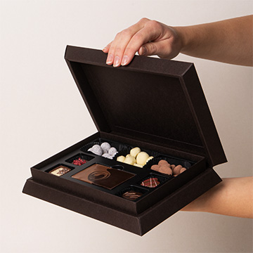 ein Set Pralinen aus belgischer Schokolade in den H&auml;nden pr&auml;sentiert